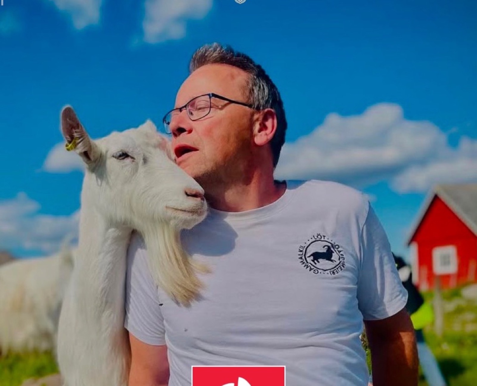 Terje Erik med en av gårdens getter mot blå himmel, med den röda ladan i bakgrunden